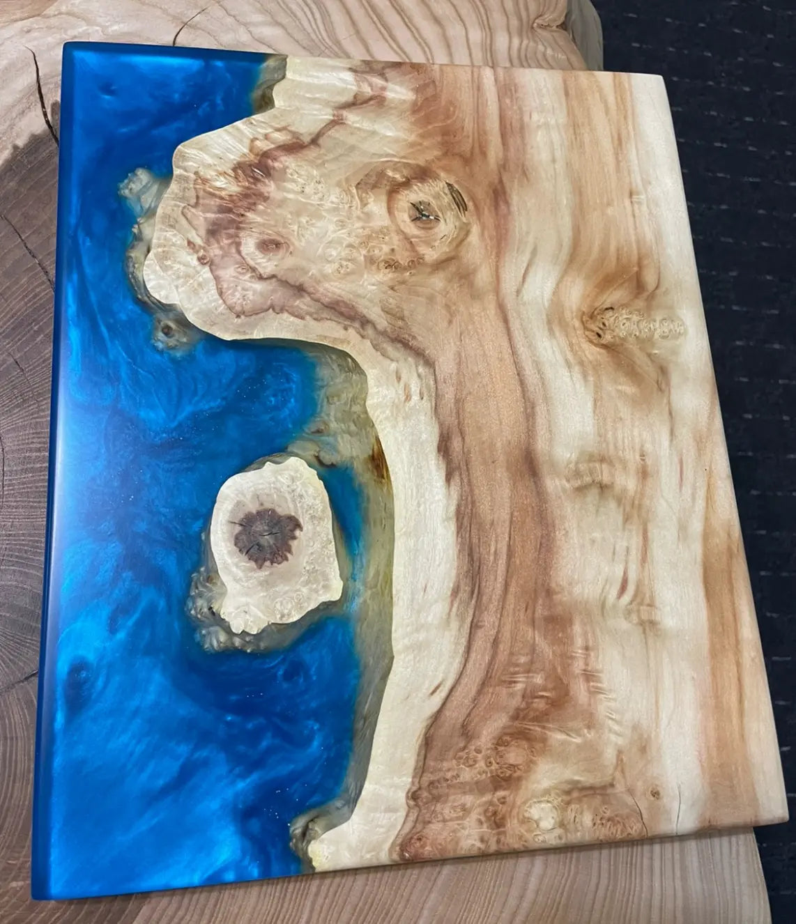 Houten snijplank met blauwe hars die doet denken aan een kustlijn. De natuurlijke nerf en knoesten van het hout creëren een aardse, artistieke sfeer die doet denken aan een vredig oceaantafereel.