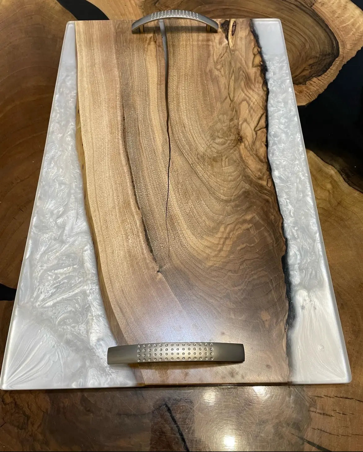 Een rechthoekig dienblad met een gepolijst houten middenstuk en witte epoxyranden. Metalen handgrepen zorgen voor een moderne touch. Het dienblad rust op een houten oppervlak.