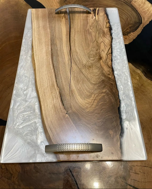 Een rechthoekig dienblad met een gepolijst houten middenstuk en witte epoxyranden. Metalen handgrepen zorgen voor een moderne touch. Het dienblad rust op een houten oppervlak.