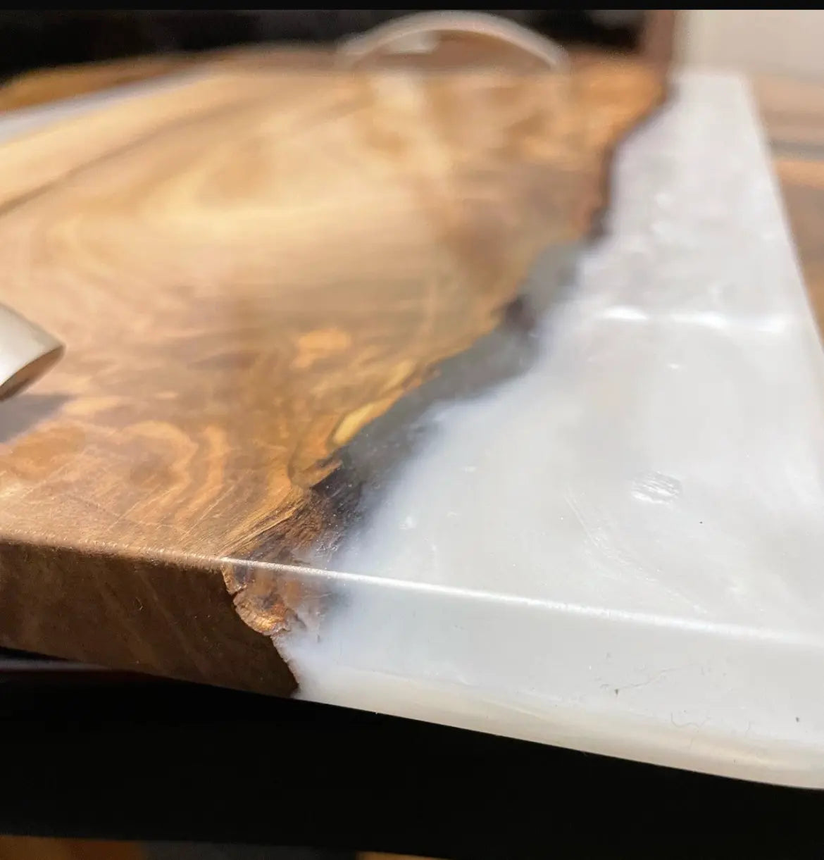 Close-up van een houten tafel met een gladde, gepolijste rand tegen een achtergrond van melkachtig wit hars. De rijke nerf van het hout contrasteert met de gladde hars, wat zorgt voor een moderne, elegante uitstraling.