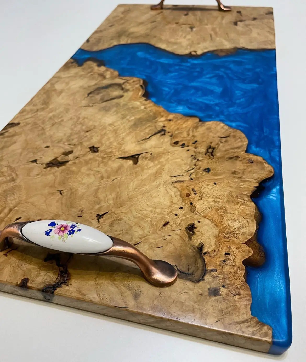 Elegante snijplank met rijke, stormachtige blauwe hars die doet denken aan een rivier en contrasteert met de natuurlijke houtnerf. Het keramische handvat met bloemmotief zorgt voor een delicate touch.