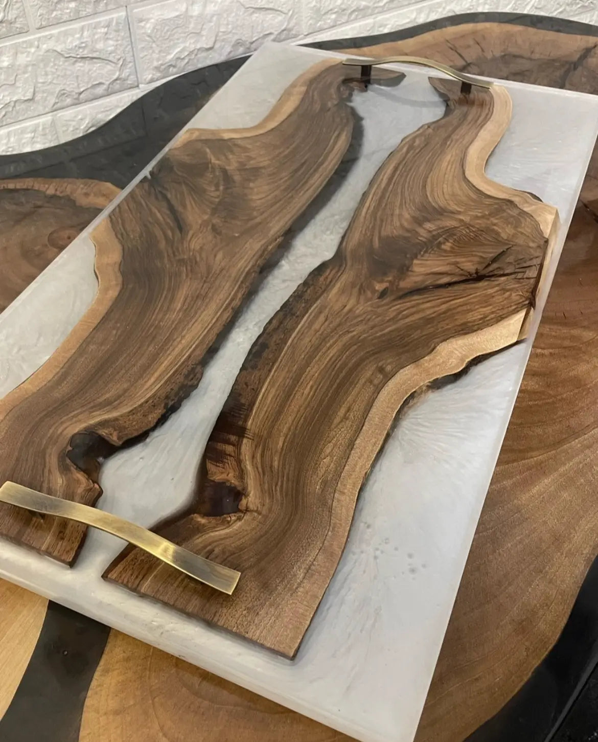 Serveerblad van hout en hars op een houten tafel. Het blad heeft een natuurlijk houtnerfpatroon met een witte harsbodem, geaccentueerd door strakke metalen handgrepen.