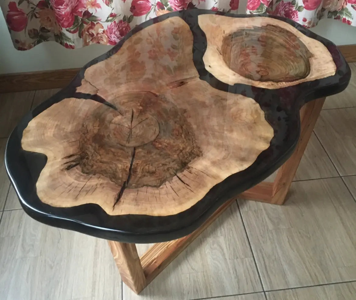 Een rustieke houten salontafel met een glanzende, zwarte harsrand accentueert de natuurlijke nerf en onregelmatige vorm van het houten blad. De warme tinten creëren een gezellige en natuurlijke sfeer.
