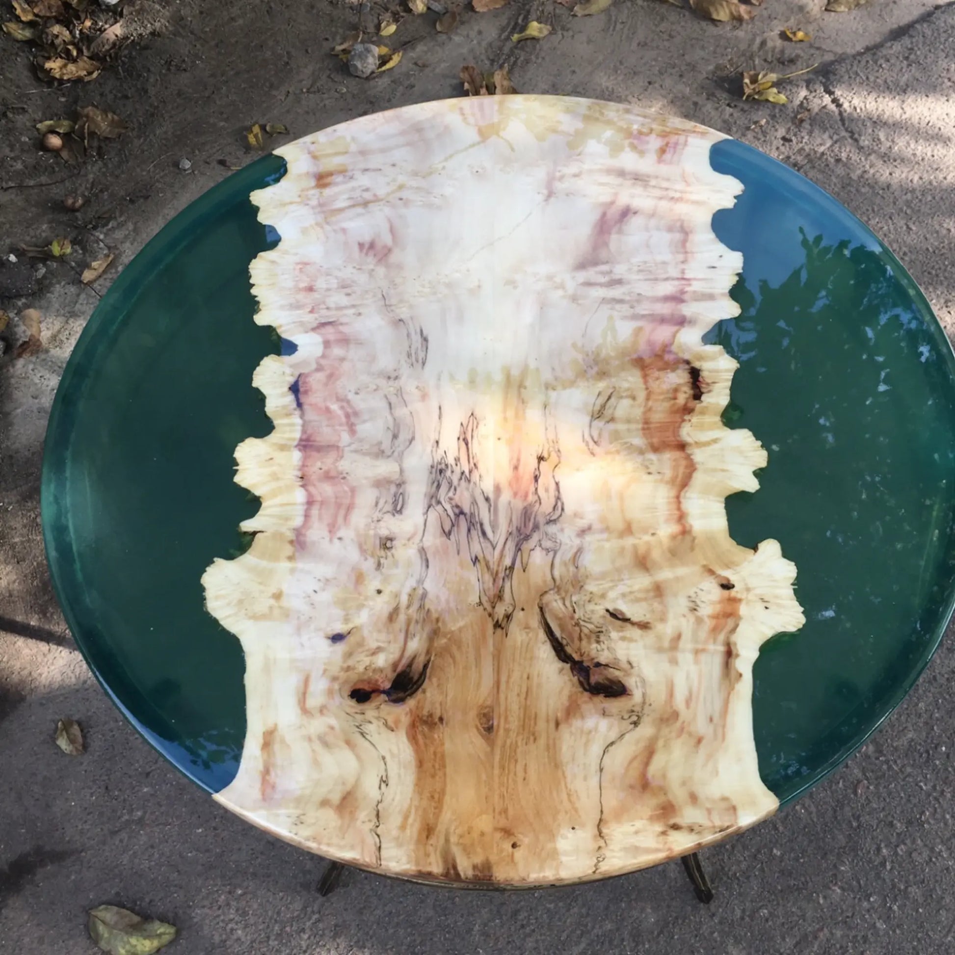 Een uniek rond tafelblad met een glad, gepolijst houten middenstuk met kleurrijke nerfpatronen, omzoomd met een glanzende groene harsrand.
