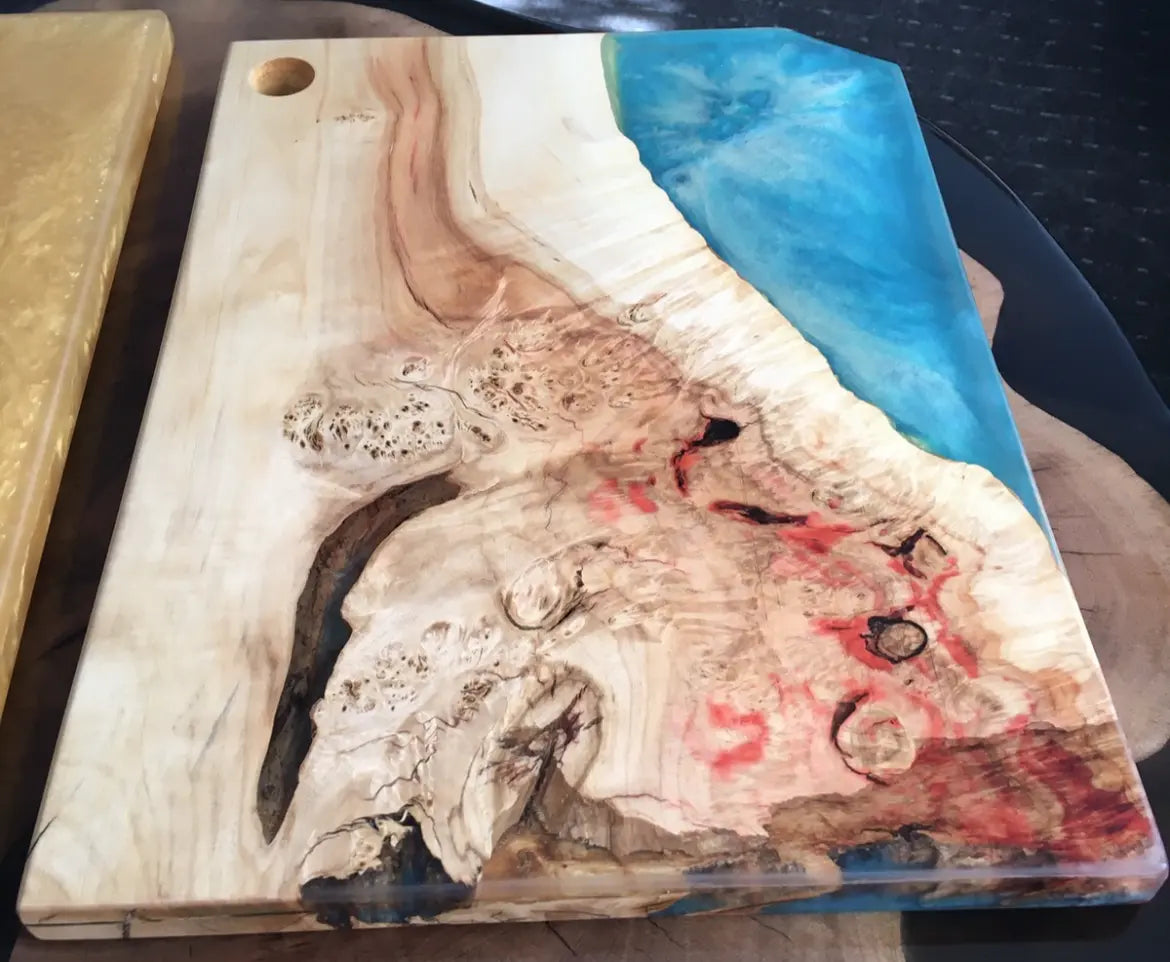 Een decoratieve houten snijplank met een levendige blauwe hars rivier op de rand, die contrasteert met de natuurlijke houtnerf en rode accenten.