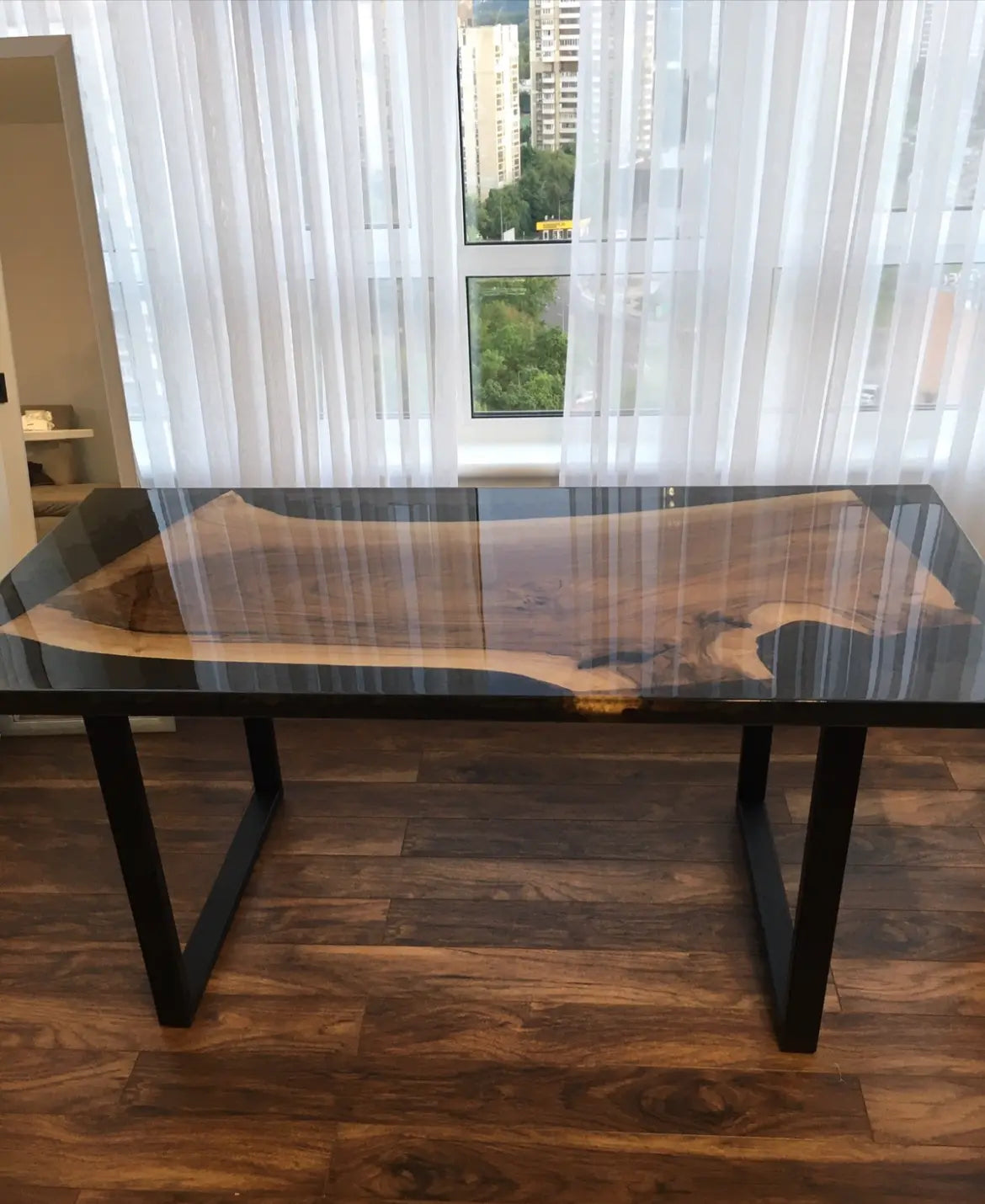 Houten tafel met natuurlijke randen en glanzende epoxylaag, opvallend houtnerfpatroon en zwarte poten – handgemaakte boomstamtafel in natuurlijk daglicht.
