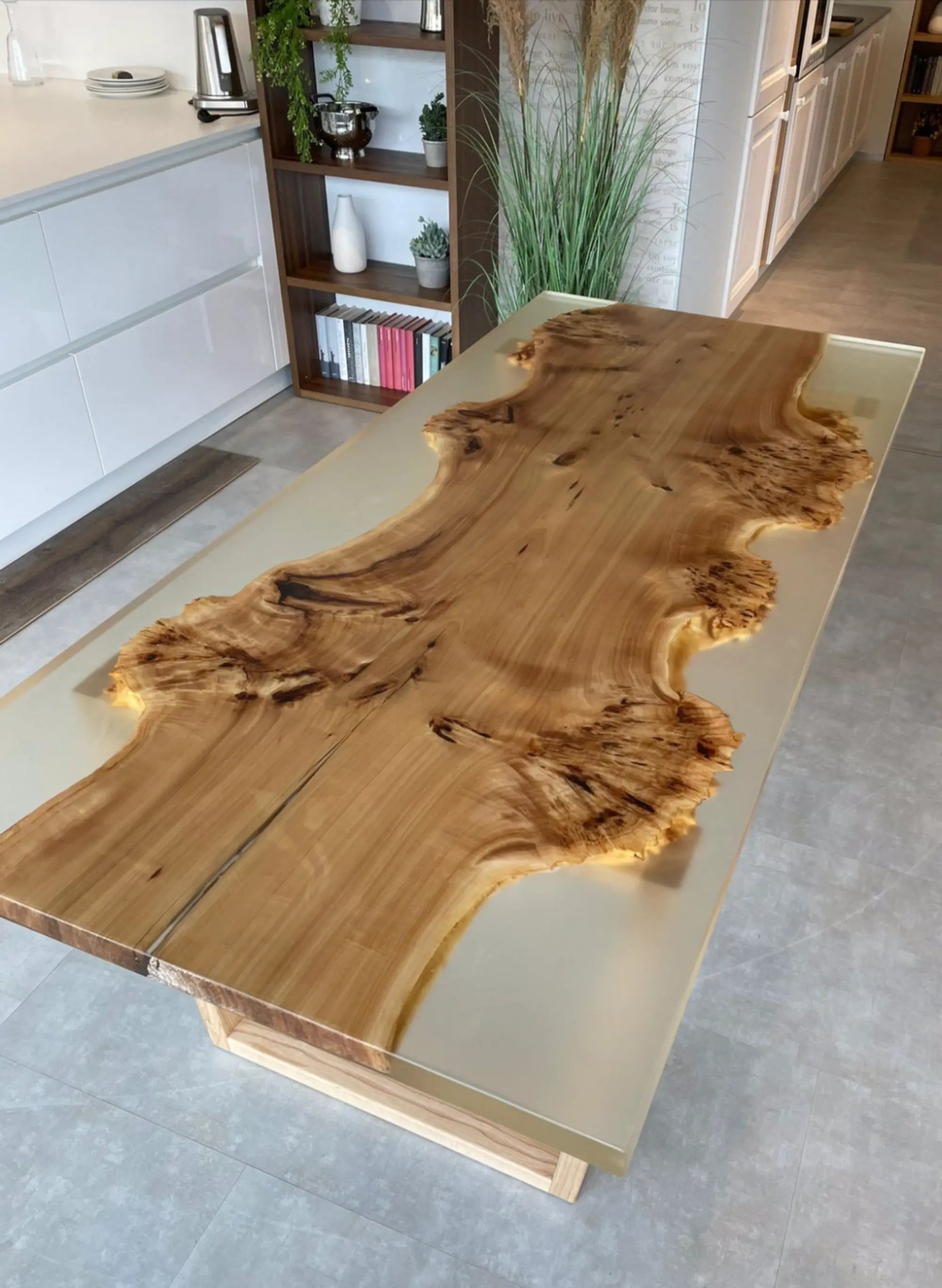 Een grote houten tafel met een natuurlijk randontwerp, een glad oppervlak met duidelijke nerfpatronen, rustend op een lichtgekleurd onderstel in een modern interieur.