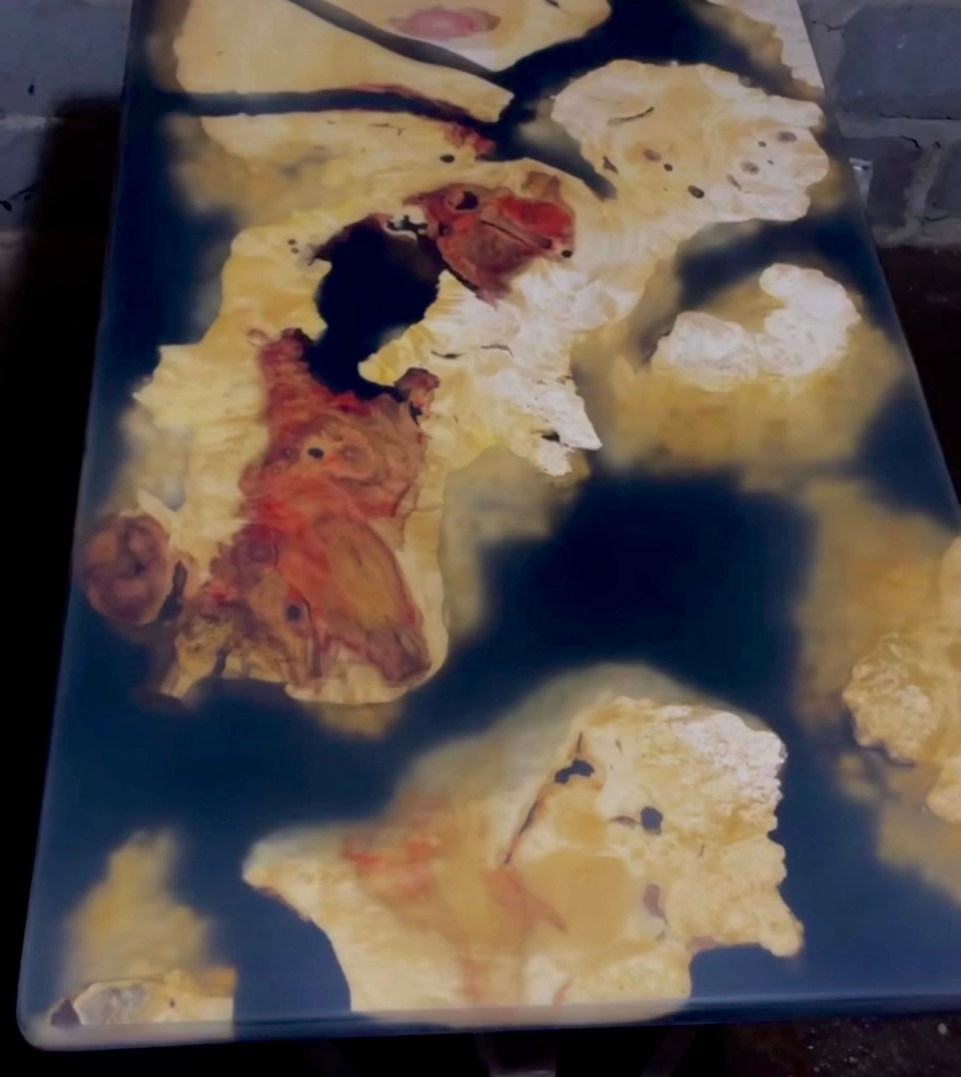 Luxe handgemaakte epoxyhars en houten salontafel met organisch live edge ontwerp, rode en crèmekleurige houtnerven in glanzende zwarte hars. Uniek designmeubel voor moderne en landelijke interieurs.