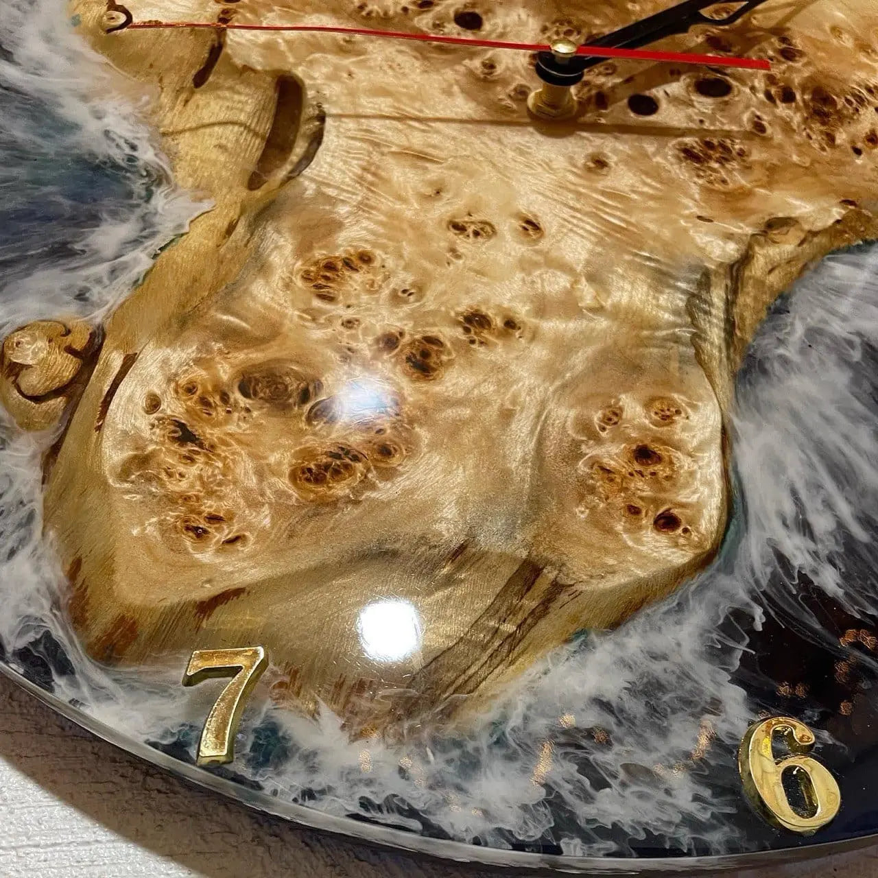 Close-up van een decoratieve klok met hout- en harsontwerp, met gouden cijfers 7 en 6 en wijzers die naar verschillende tijden wijzen.