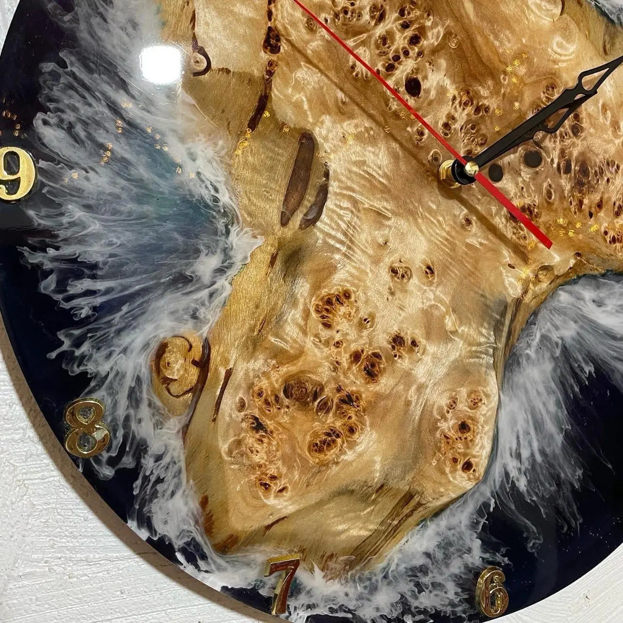 Close-up van een klok van hout en kunsthars, met wervelende witte en zwarte patronen en gouden cijferdetails. De wijzers zijn zwart en rood.