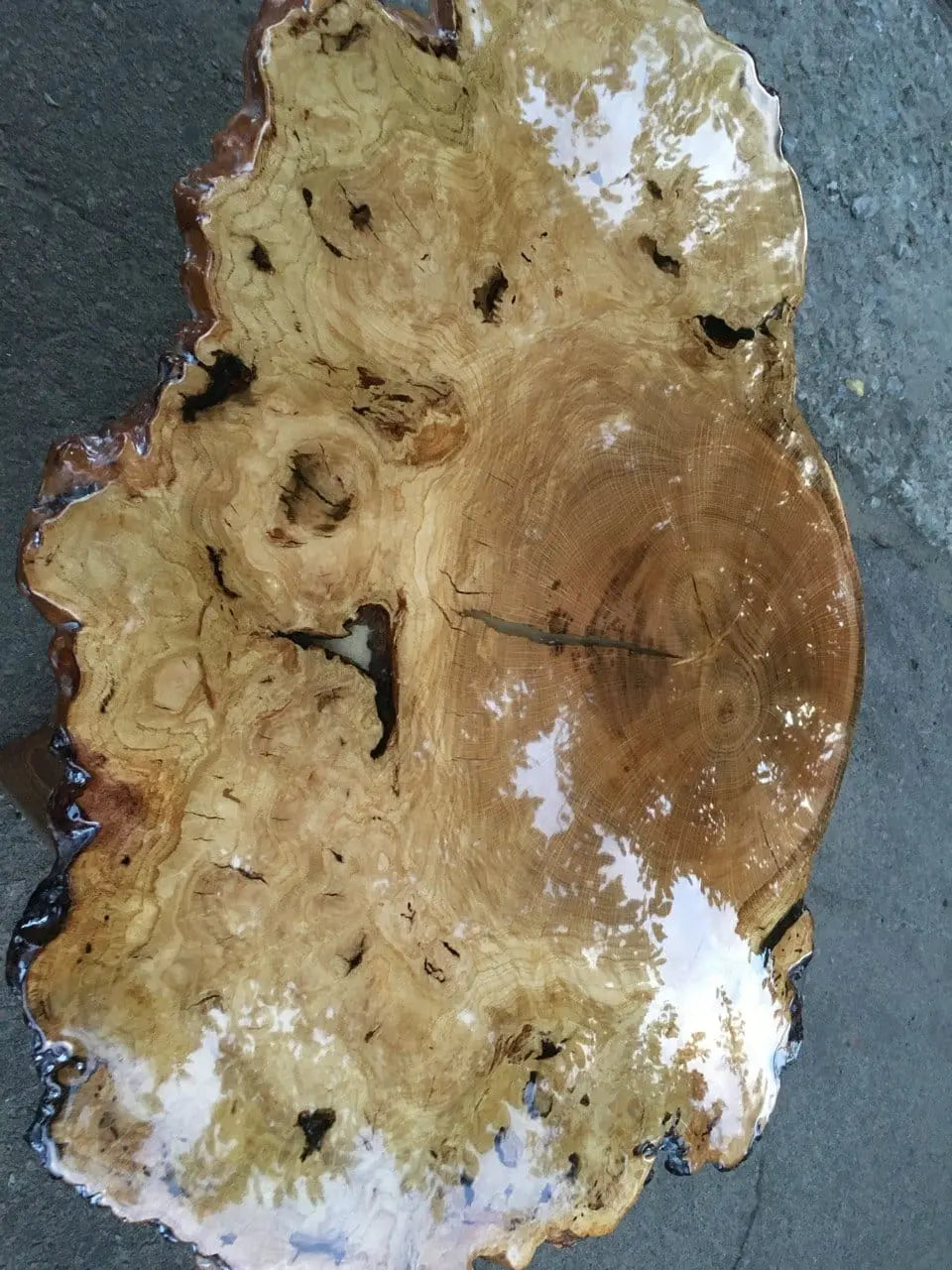Close-up van een gepolijste houten tafel met rijke natuurlijke patronen en een glanzende afwerking die het licht reflecteert. De organische vorm van de tafel voegt een rustieke charme toe.