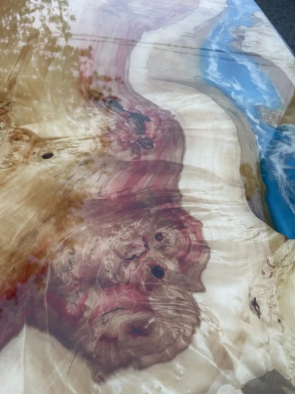 Close-up van een kleurrijke tafel van epoxyhars met wervelende patronen. Rode, beige en blauwe tinten imiteren een rivier die door een natuurlijk landschap stroomt. Glanzend oppervlak.