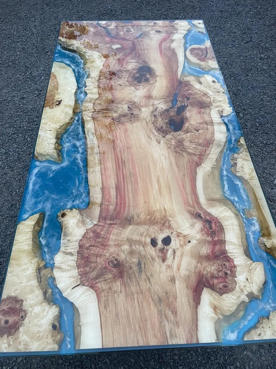 Tafel van hout en hars met een vloeiend blauw riviermotief op een grindoppervlak. De natuurlijke houtnerf heeft warme tinten en knoesten.