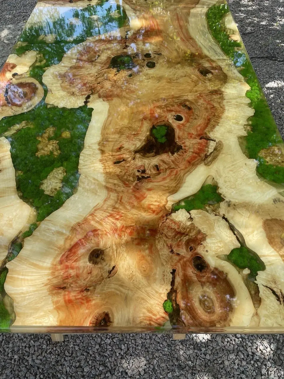 Gladde, gepolijste houten tafel met wervelende oranje, bruine en crèmekleurige nerven, geaccentueerd door levendig groen kunsthars. Reflecterend oppervlak met gevlekt licht.