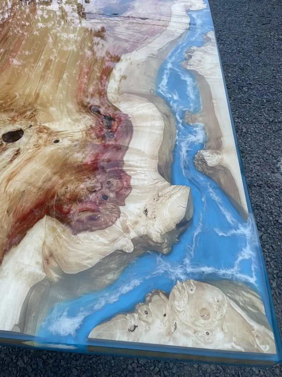 Close-up van een tafel van hars en hout, met wervelende patronen van natuurlijk hout met levendig blauw en wit hars dat lijkt op een rivier, wat een serene, artistieke sfeer oproept.