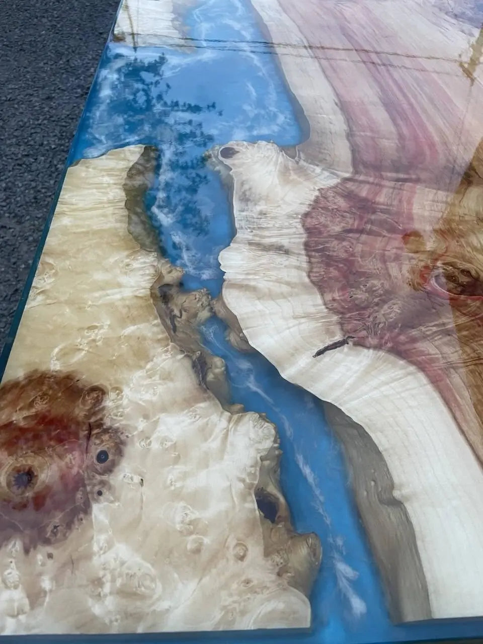 Het gladde tafelblad combineert natuurlijke houtnerven met levendig blauw hars, wat doet denken aan een rivier. Het glanzende oppervlak weerspiegelt wolken en roept een sereen landschap op.