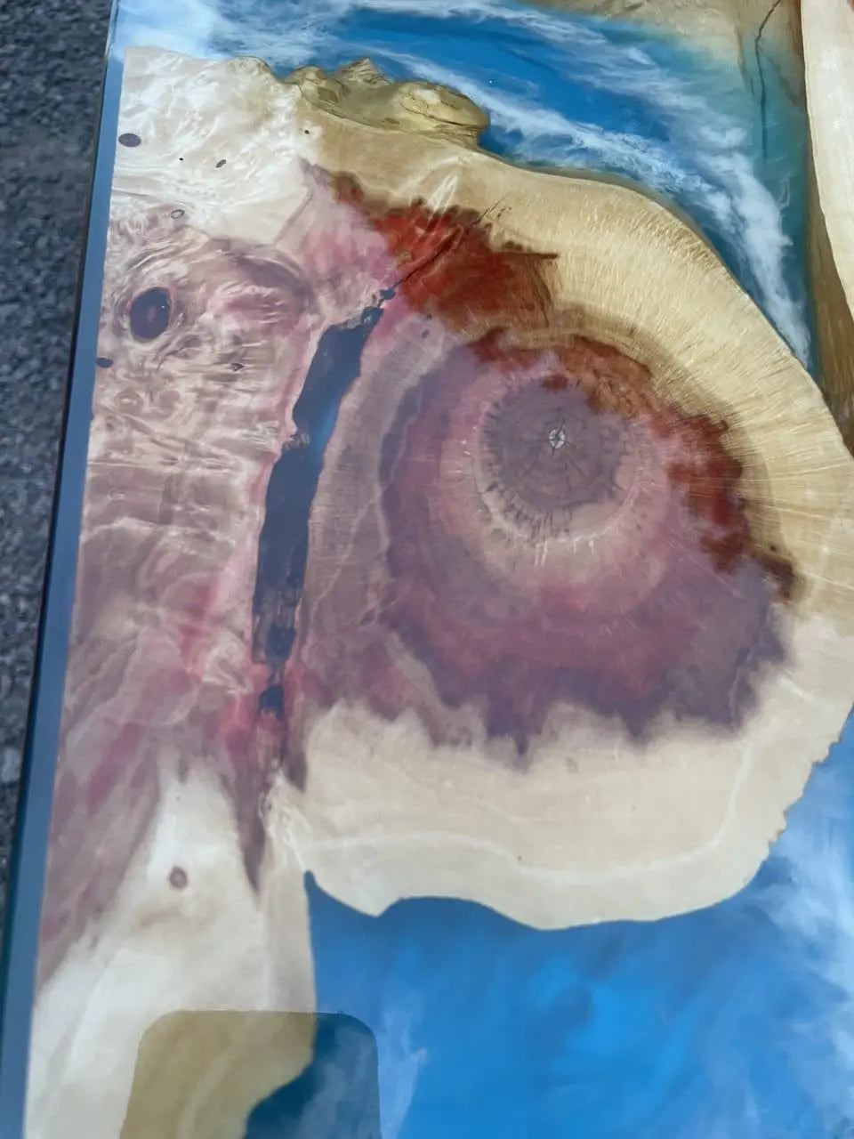 Close-up van een blauwe tafel van hars en hout, met wervelende patronen en natuurlijke houtnerf met rode en beige tinten.