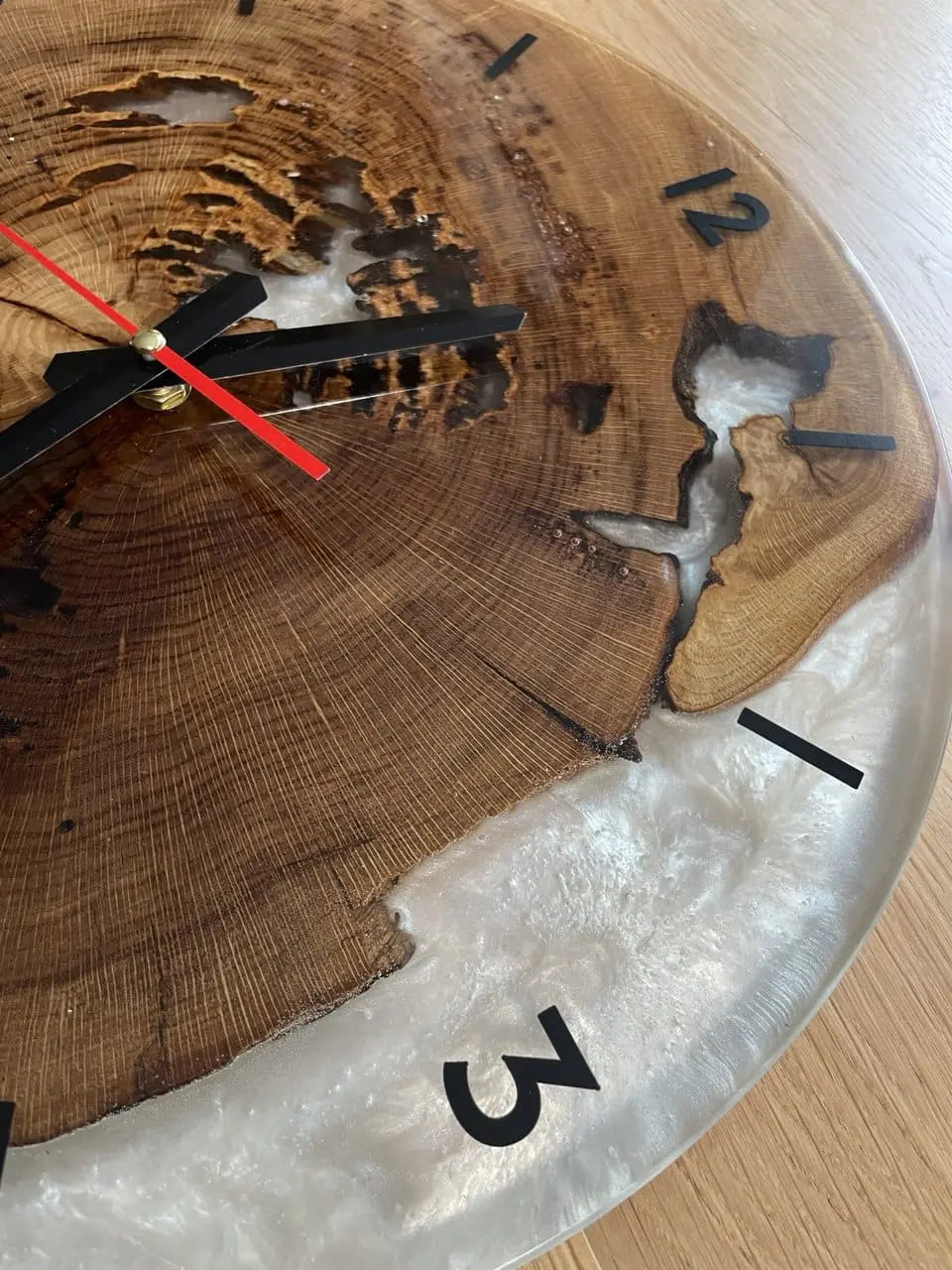 Wandklok van hout en kunsthars met zwarte cijfers en wijzers op een houten achtergrond. Rode secondewijzer, rustieke stijl en elegant design.