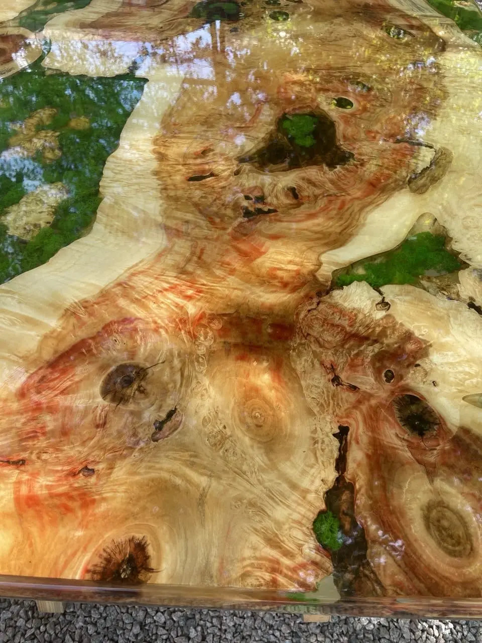 Close-up van een gepolijste houten tafel met wervelende nerfpatronen in warme tinten oranje, beige en bruin. Groene mosaccenten zorgen voor een natuurlijke touch.