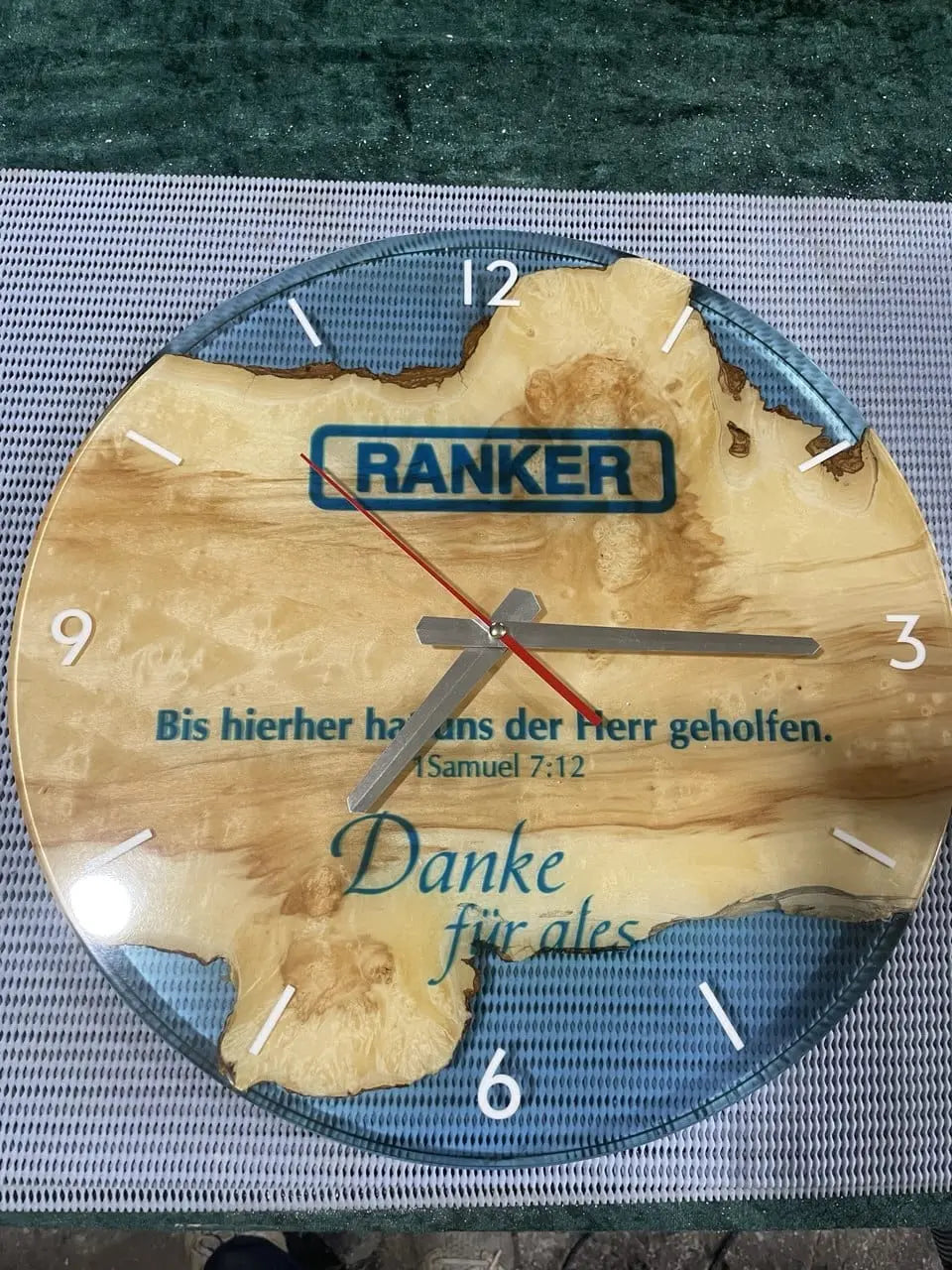Handgemaakte houten wandklok met blauwe epoxyhars accenten, zilverkleurige wijzers, rode secondewijzer en witte cijfers. Uniek design met Duitse gravure over dankbaarheid. Moderne rustieke klok voor woonkamer, kantoor of cadeau.