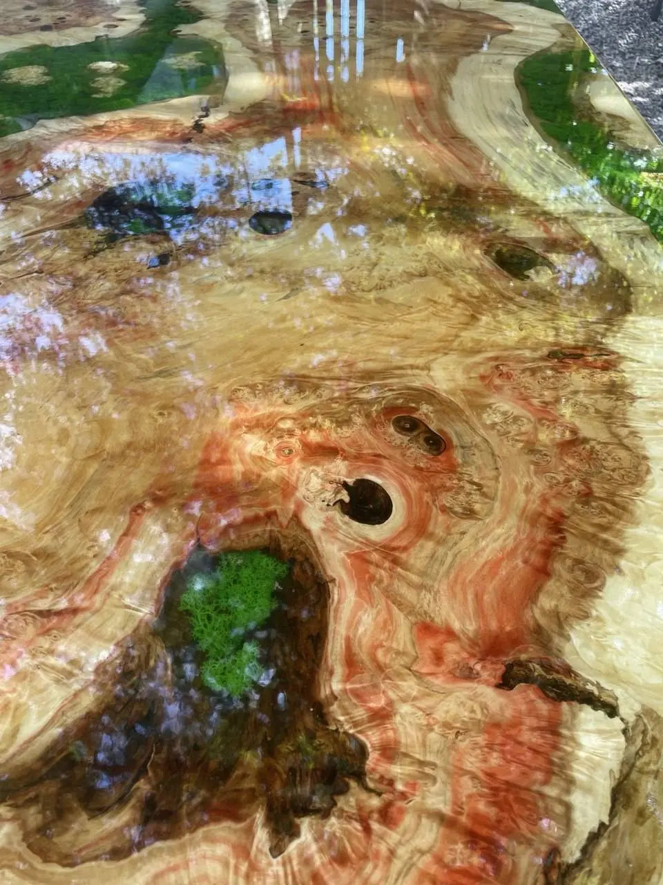 Wervelende patronen van gepolijst hout met levendige rode en groene tinten, met reflecterende patches en ronde openingen, creëren een dynamisch, natuurlijk, abstract kunsteffect.