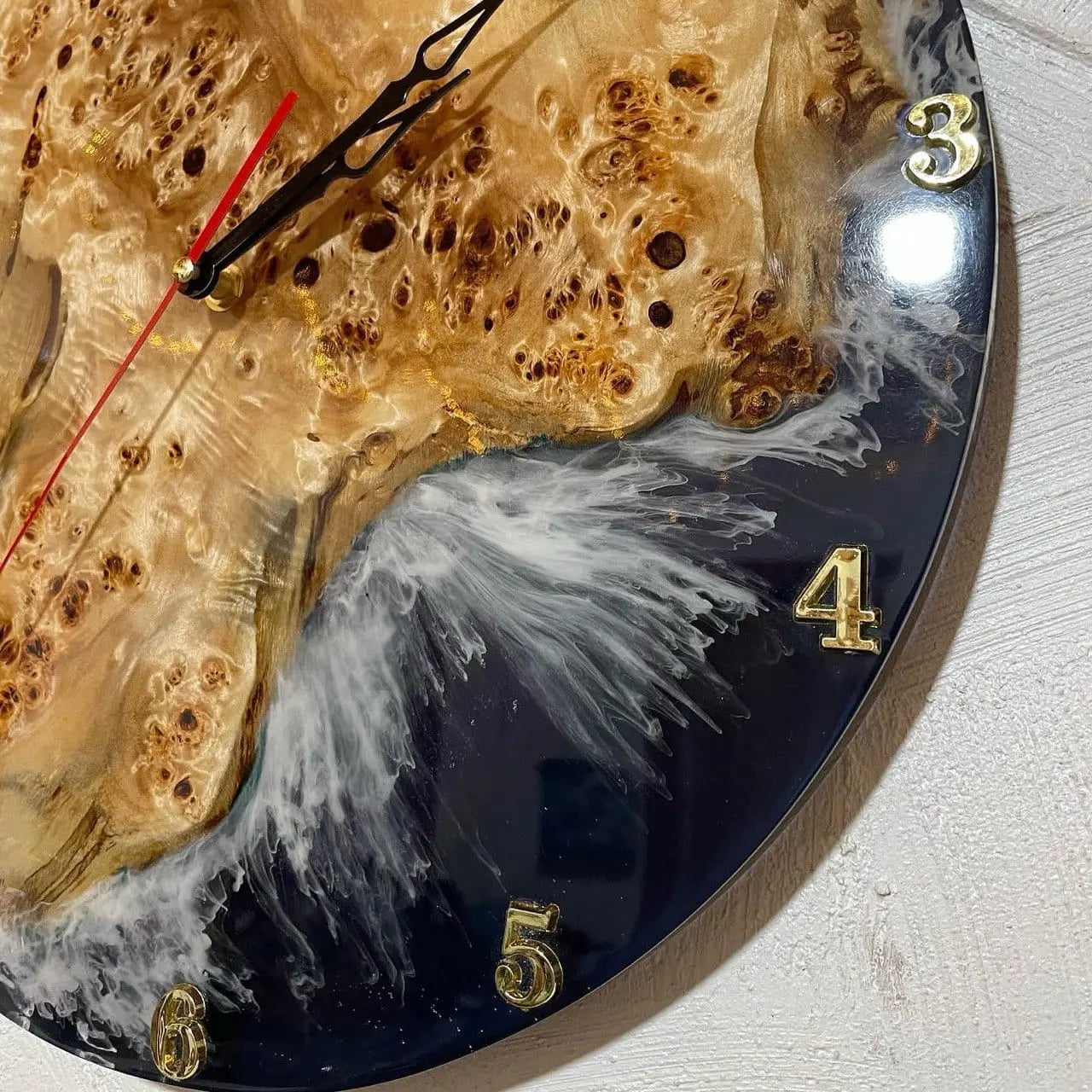 Close-up van een decoratieve wandklok met een wijzerplaat van hout en hars. De klok heeft gouden cijfers en witte slierten die door diepzwart hars wervelen.