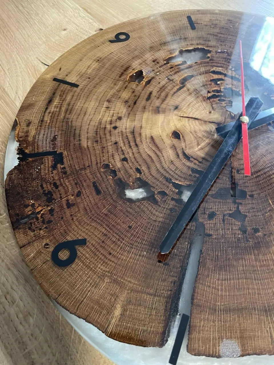 Close-up van een rustieke wandklok gemaakt van een boomstam met zichtbare ringen. Zwarte cijfers en wijzers contrasteren met de natuurlijke houtnerf.