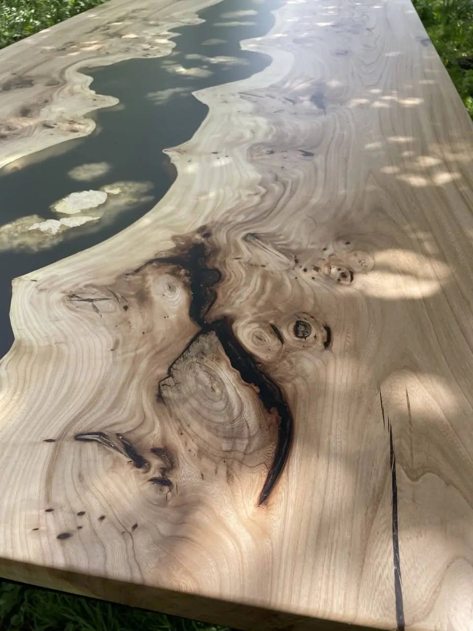 Close-up of a wooden tabletop with a smooth, natural grain and a river-like resin inlay. The wood has swirling patterns and knots, creating an organic and artistic look.
