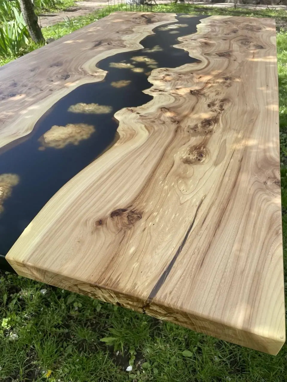 Handmade wooden river table with black epoxy inlay, featuring rich natural wood grain and rustic knots.