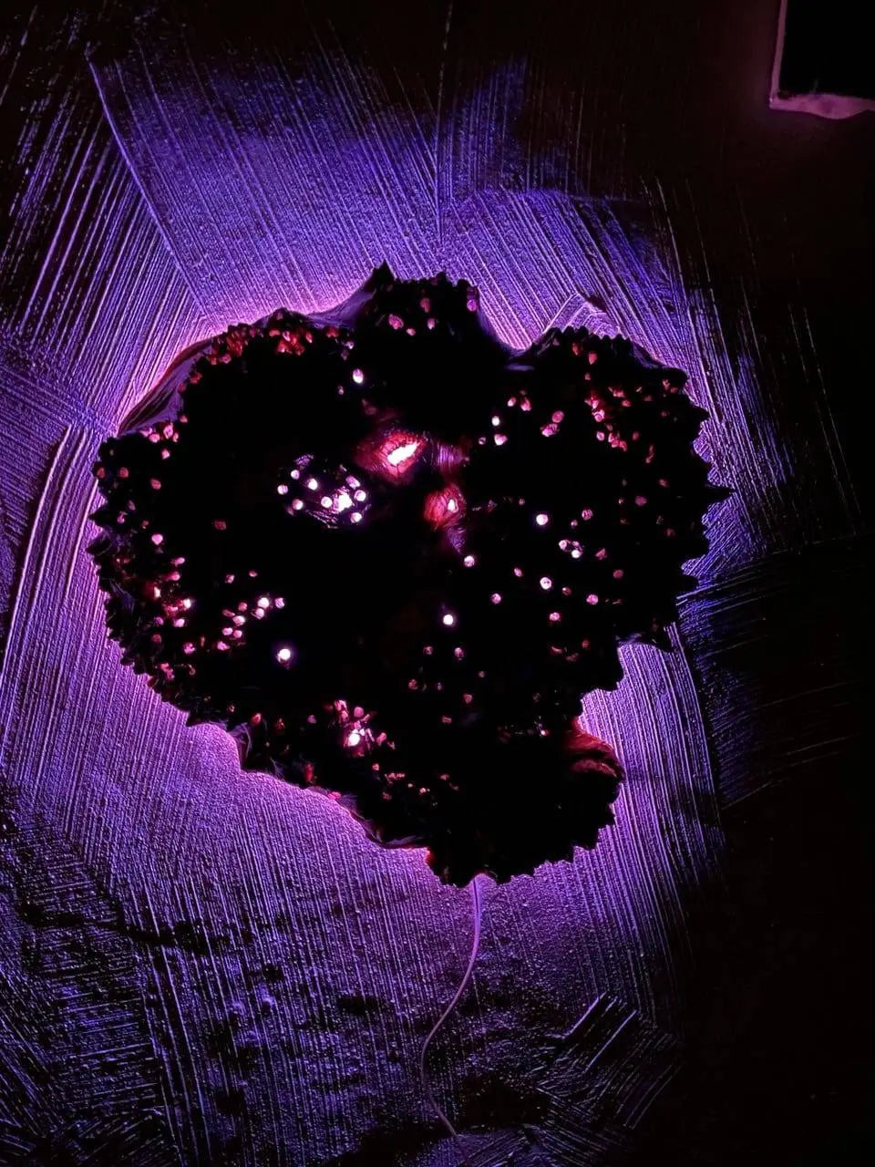 Een levendige cluster van dieproze lichtjes vormt een abstract hart op een getextureerd, verlicht paars oppervlak, waardoor een mystieke en intrigerende sfeer ontstaat.