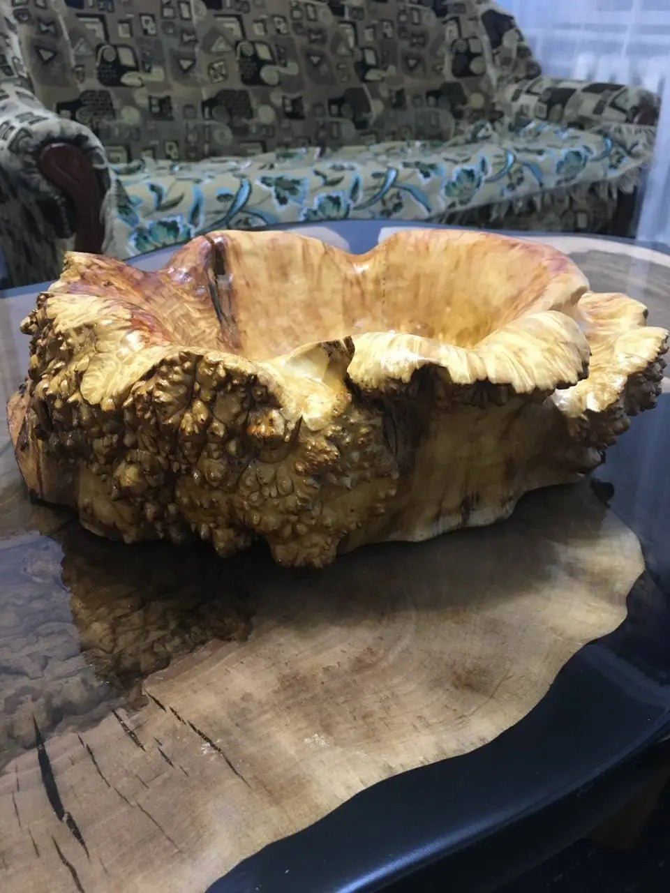 Een grote, houten kom met ingewikkelde natuurlijke patronen staat op een gepolijste houten tafel.