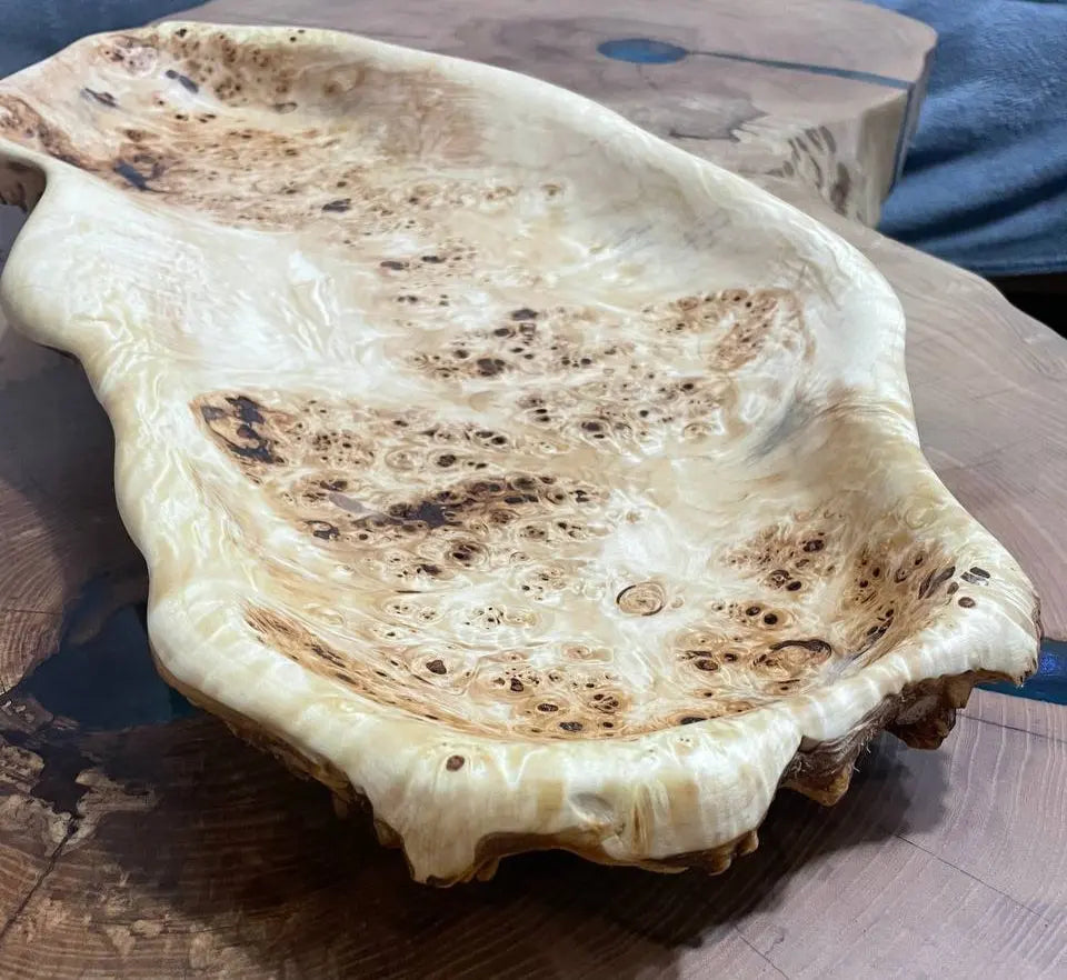 Handgemaakte houten schaal met ingewikkelde, wervelende patronen en een glanzende afwerking op een ronde houten tafel.