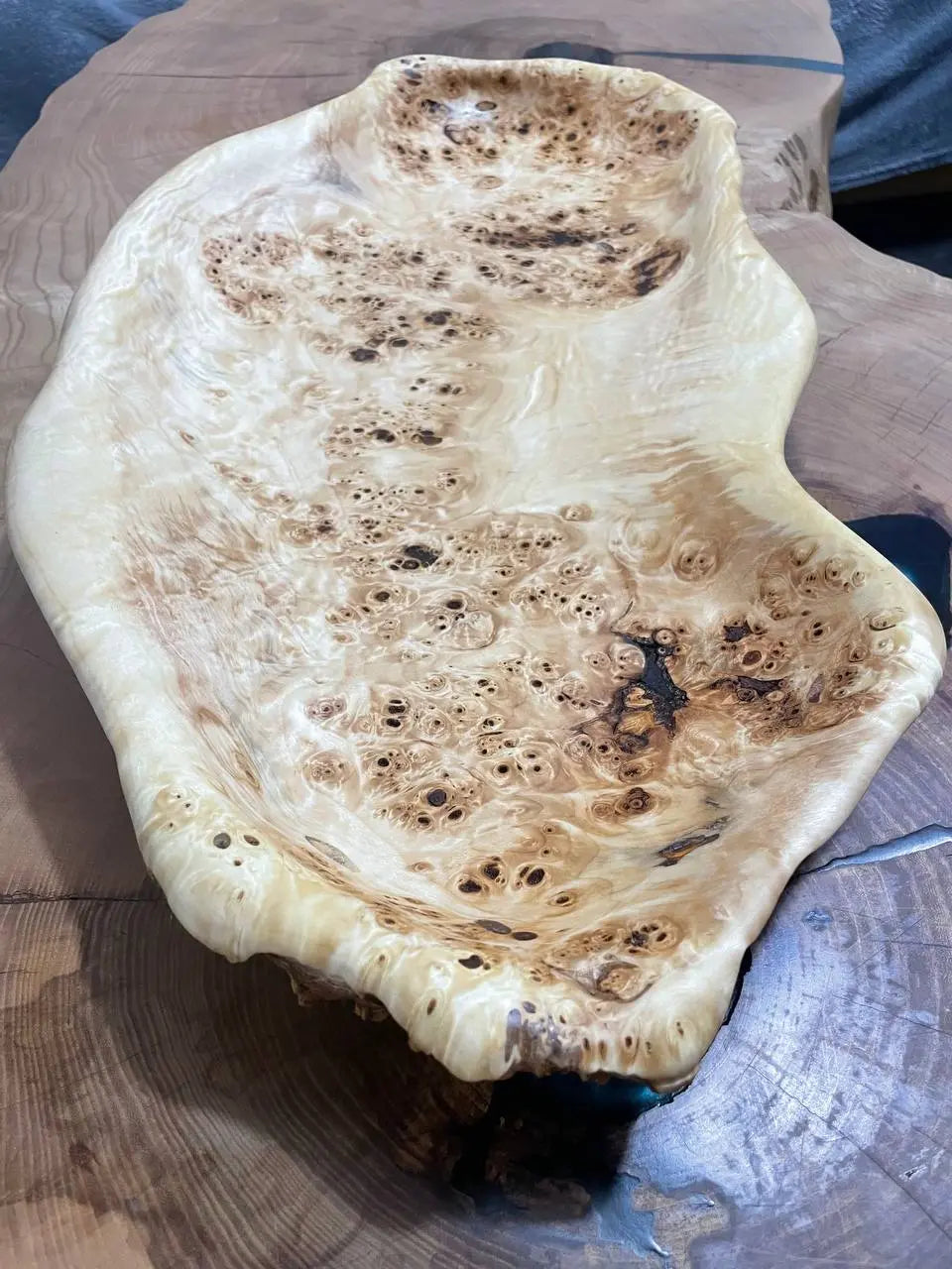 Een glad, ingewikkeld gepatroneerd houten schaaltje met een rijke, geknoopte textuur, geplaatst op een donker houten oppervlak, straalt een natuurlijke en artistieke elegantie uit.