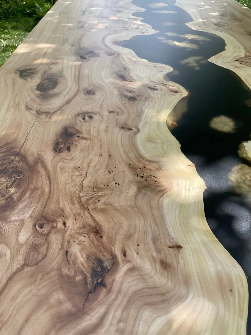 Close-up of a luxury wood and epoxy resin river table, featuring detailed natural wood grain and a glossy black resin stream. Perfect for modern interiors, handcrafted for a unique and artistic furniture statement.