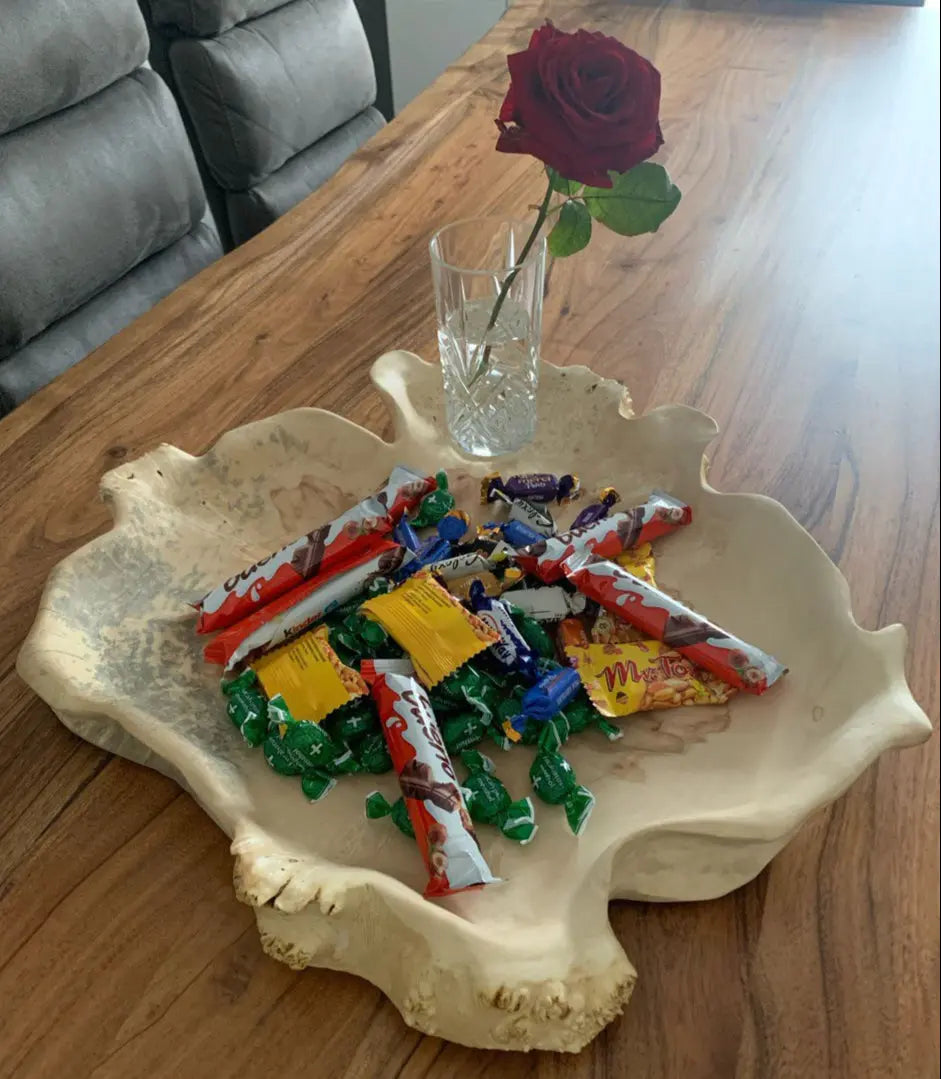 Bovenaanzicht van een bladvormige schaal kom van esdoornhout voor tafeldecoratie met chocolaatjes en een glas met rode roos.