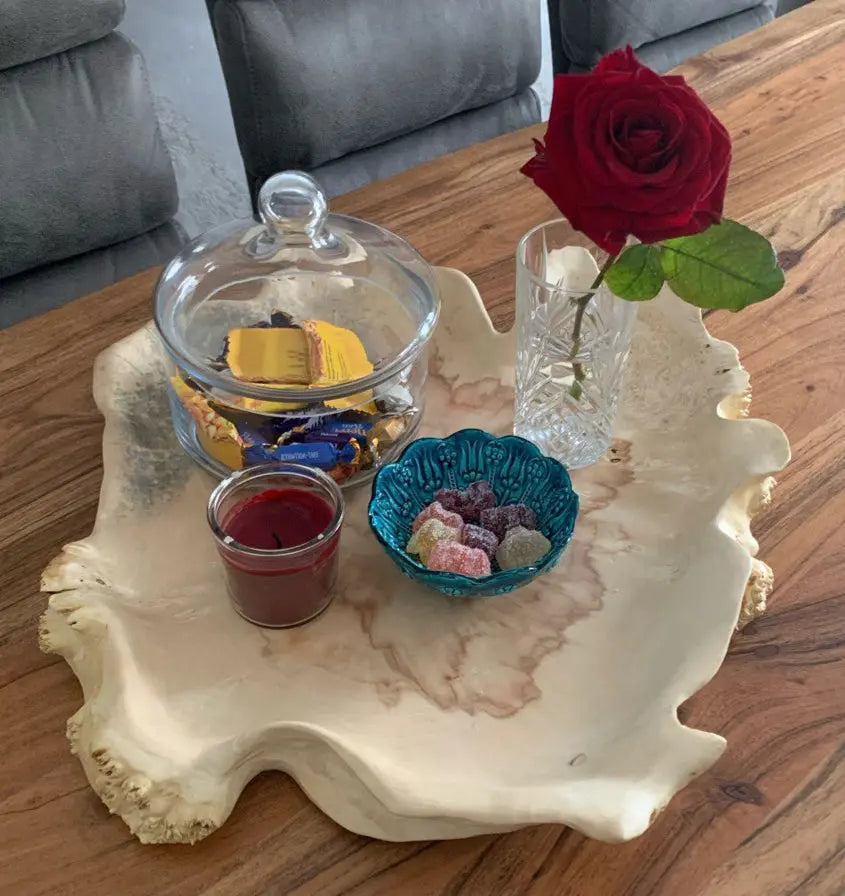 Bovenaanzicht van een bladvormige schaal van esdoornhout voor tafeldecoratie met verschillende maten kleine glazen potjes.