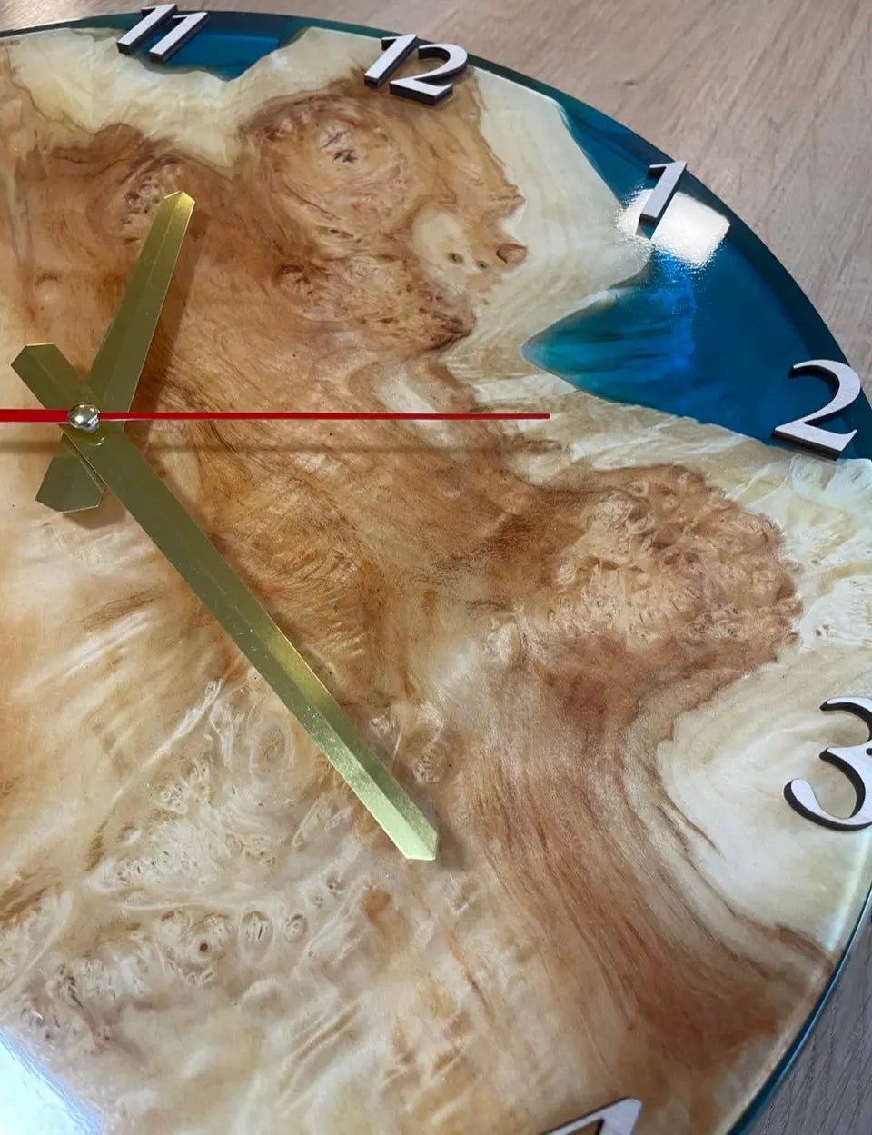 Inzoomen op een handgemaakte decoratieve ronde analoge wandklok van wortelhout en levendige oceaanblauwe epoxyhars.