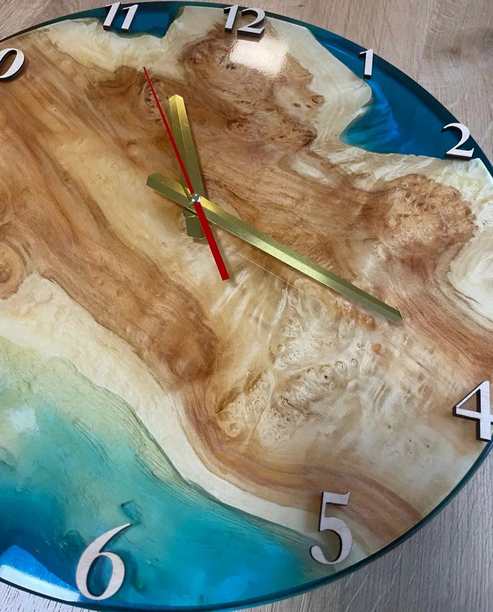 Inzoomen op wandklok gemaakt van wortelhout en levendige oceaanblauwe epoxyhars met gouden en rode wijzers.
