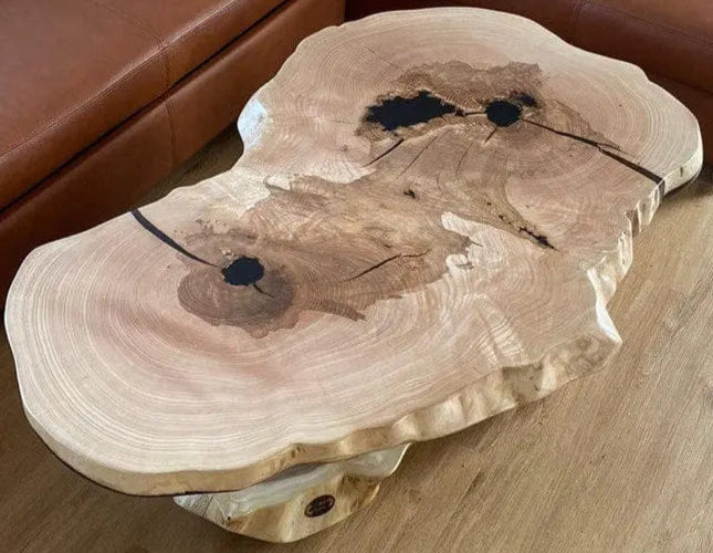 Een uniek gevormde houten salontafel met een natuurlijke, rustieke uitstraling. Hij is voorzien van donkere ingelegde knopen en nerfpatronen, wat een aardse, artistieke sfeer oproept.