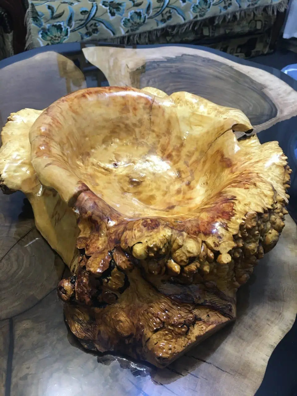 Zeer gepolijst houten beeld met een glanzend, gestructureerd oppervlak dat lijkt op natuurlijk wortelnotenhout, geplaatst op een ronde houten tafel. Aardse tinten, organische vorm.