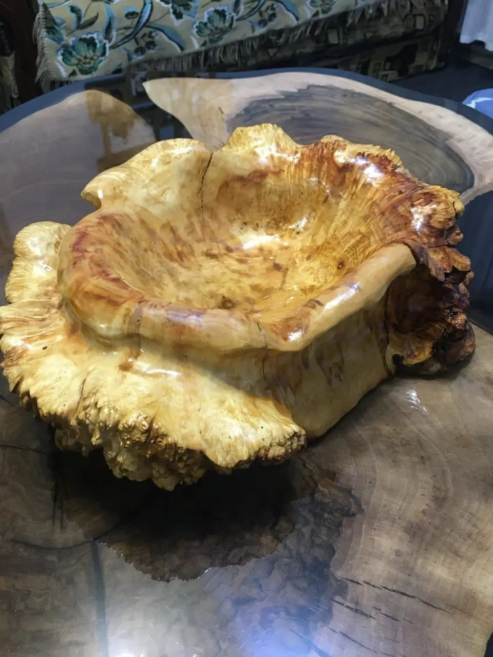 Een zorgvuldig gesneden houten kom met rijke, gouden tinten en een organische textuur, rustend op een gepolijste houten tafel.
