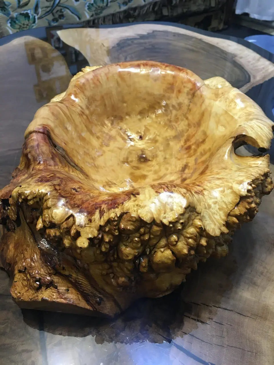 Kom van wortelnotenhout op een glazen tafel, met een glanzend, gestructureerd oppervlak met ingewikkelde patronen in warme goud- en bruintinten. Natuurlijke elegantie.