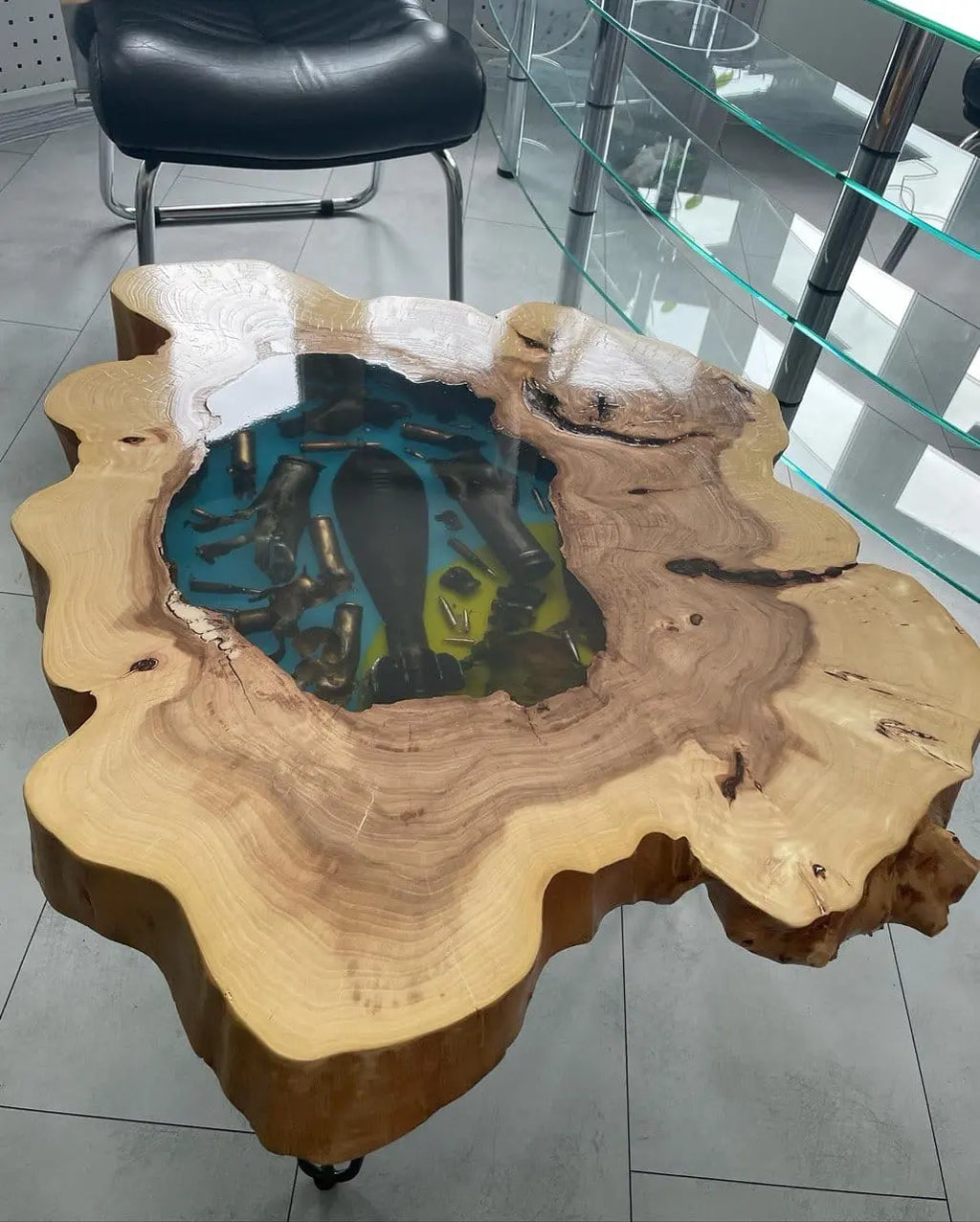 Handgemaakte rustieke houten salontafel met natuurlijke boomstamrand en kleurrige epoxy inleg met echte kogelhulzen en bomscherven. Uniek designmeubel op een industriële betonnen vloer.