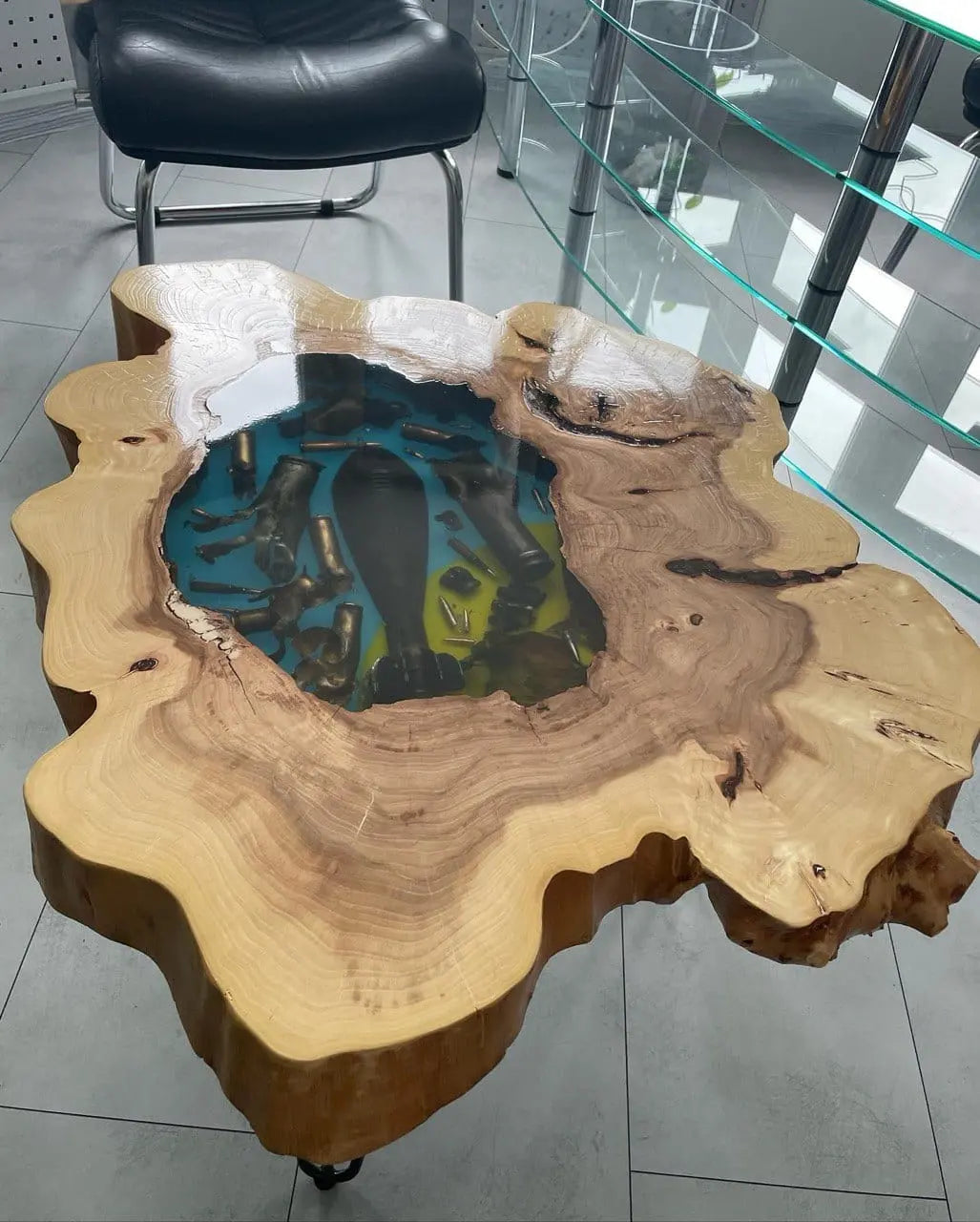 Handgemaakte rustieke houten salontafel met natuurlijke boomstamrand en kleurrige epoxy inleg met echte kogelhulzen en bomscherven. Uniek designmeubel op een industriële betonnen vloer.