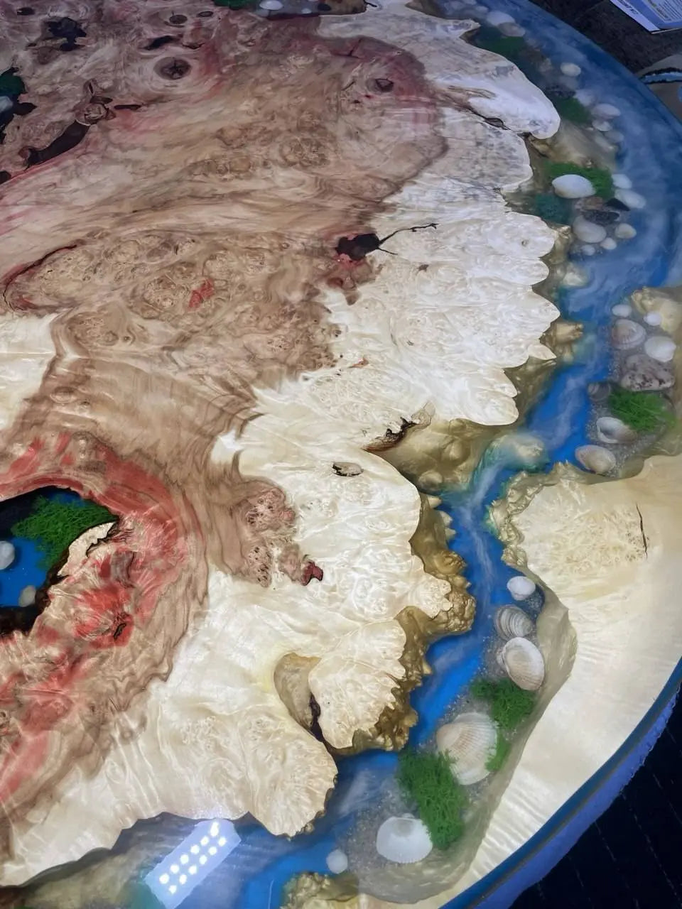 Abstracte kunst met een wervelende mix van beige, rode en bruine houtachtige texturen met een glanzende afwerking. Blauwe kunsthars imiteert een rivier, omzoomd door schelpen en groene vlekken, wat een natuurlijke, vloeiende esthetiek creëert.