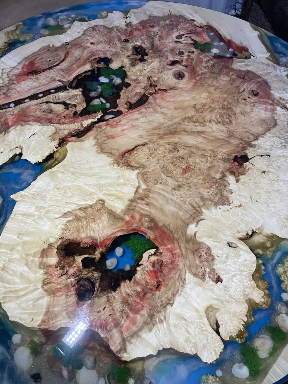 Een close-up van een epoxytafelblad met ingelegde zeeschelpen en groen mos in een wervelend, meerkleurig houtnerfpatroon, wat een natuurlijk en artistiek ontwerp creëert.