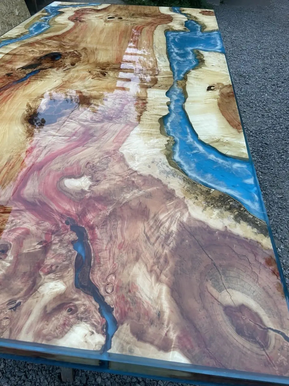 Een houten tafel met een gepolijst oppervlak met ingewikkelde natuurlijke patronen. Blauwe harsrivieren contrasteren met warme houttinten, wat een uniek, artistiek effect creëert.